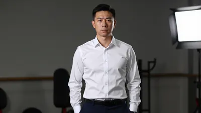 A 30-year-old male coach with a serious expression, wearing a white shirt with a smooth, unbroken fabric, and a pair of...