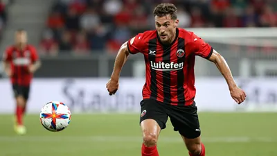 A dynamic action shot of a KV Mechelen player in a red and black striped jersey, sprinting with the ball during the match...