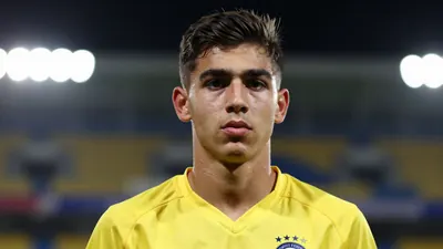 Photorealistic head-and-shoulders of a lean 18-year-old male striker in a solid yellow jersey, blurred stadium background
